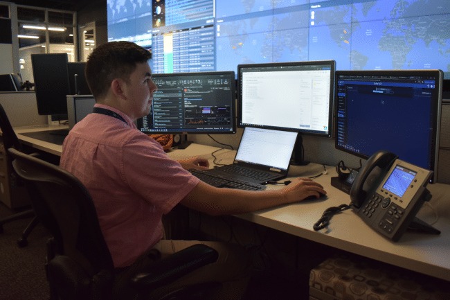 man at his desk with three computer monitors and an office phone
