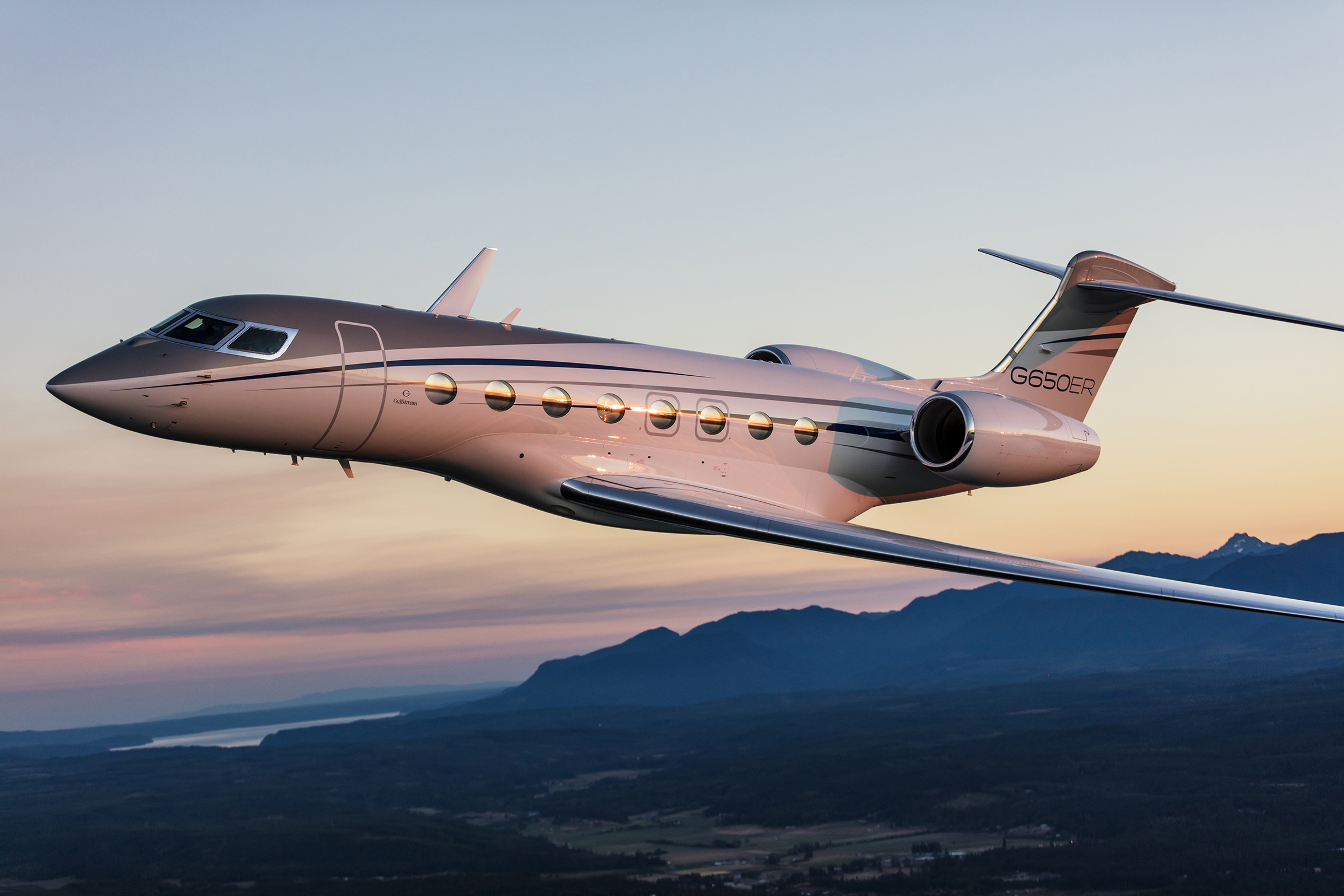 Gulfstream G650 flying in valley surrounded by mountains