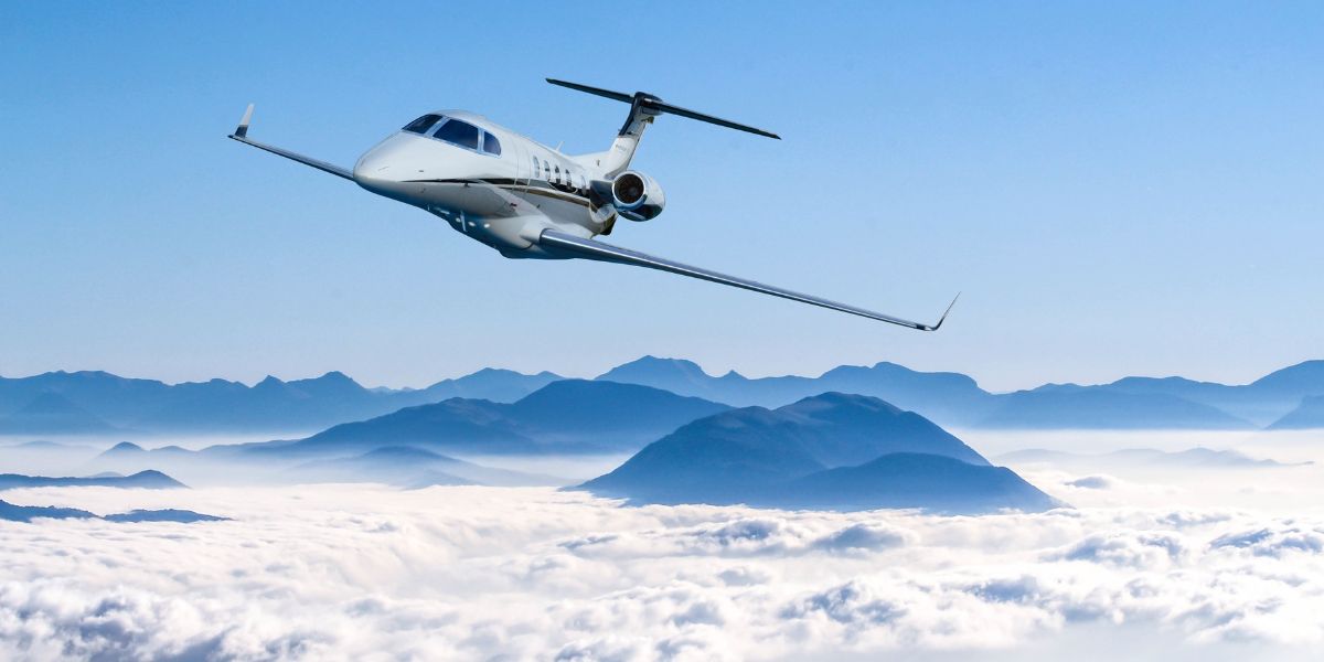 Embraer Phenom 300 flying over mountains peeking out of the clouds