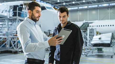 Two men inside hangar looking at tablet